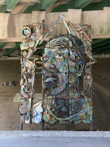 A sculpture using recycled metals depicts the face of a man looking up.