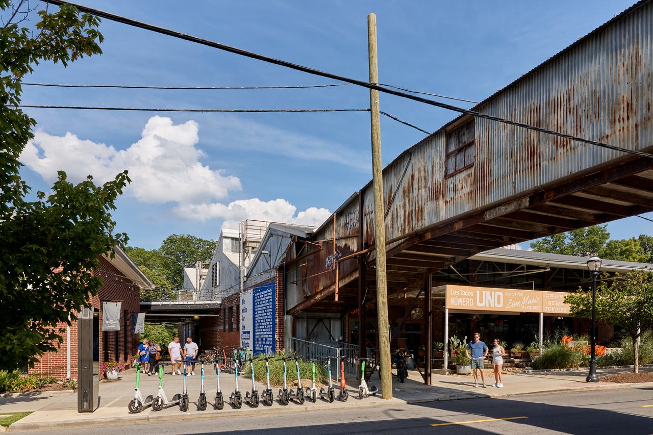 Several pedestrians stand in front of Krog Street Market and several e-scooters on a sunny day. (Photo Credit: The Sintoses)