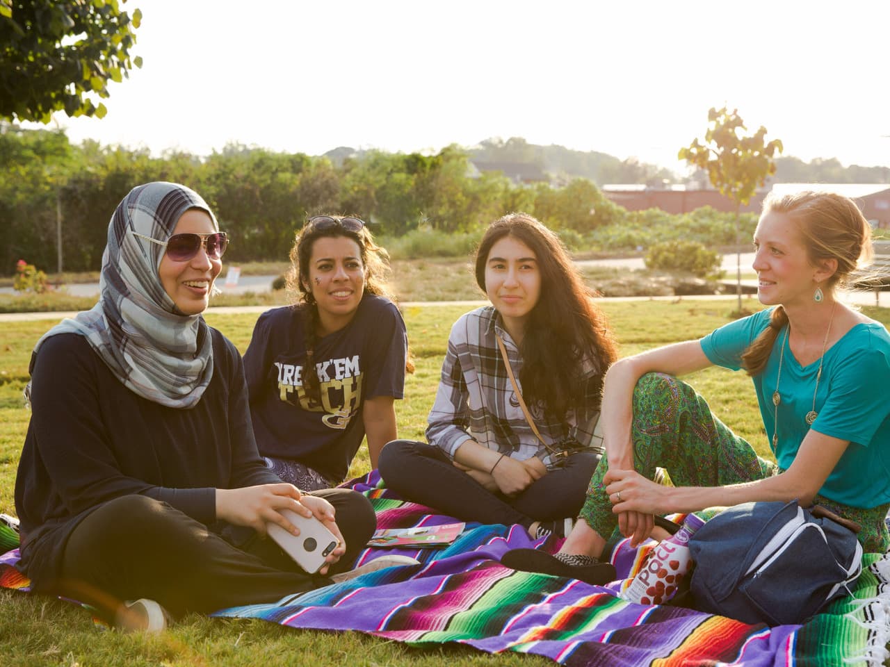 A group of girls sit on a picnic blanket together, smiling.