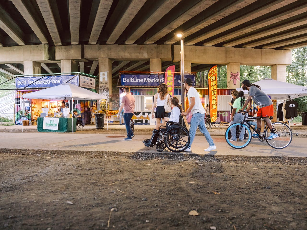 A person in a wheelchair, a person on a bike, and people walking pass by shipping container stores.