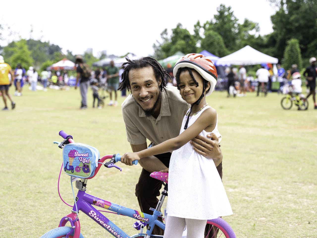 A man and a young girl stand smiling next to a bike.
