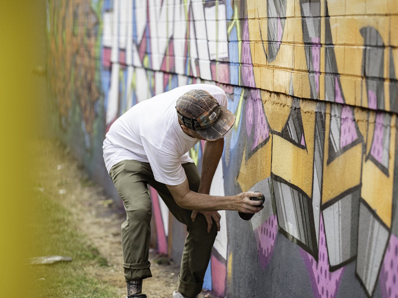 A man stands with a can of spray paint in front of a painted wall he's working on.