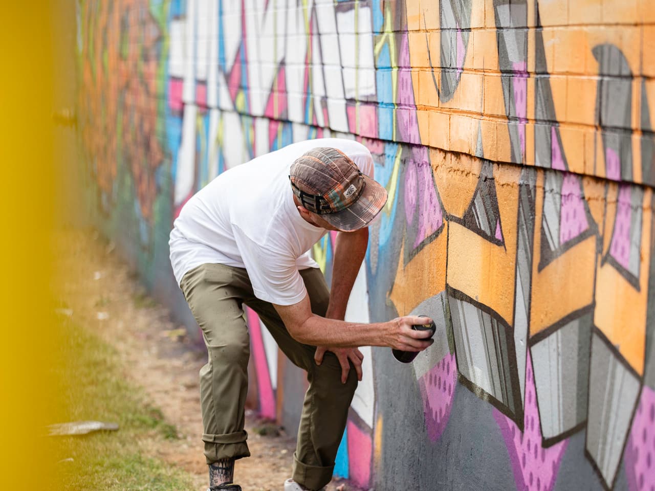 A man stands with a can of spray paint in front of a painted wall he's working on.