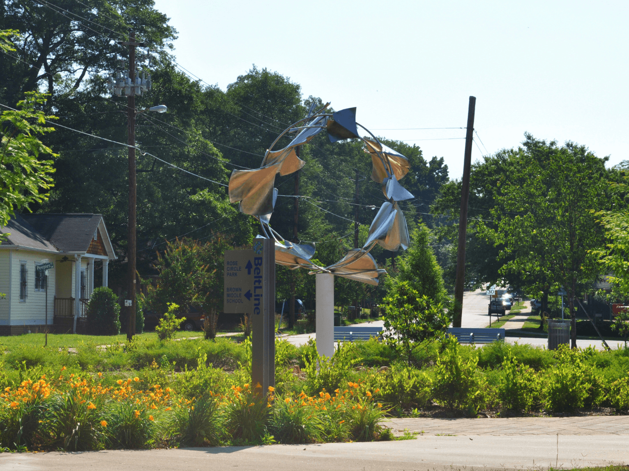 A massive metal ring sculpture sits in a garden surrounded by trees.