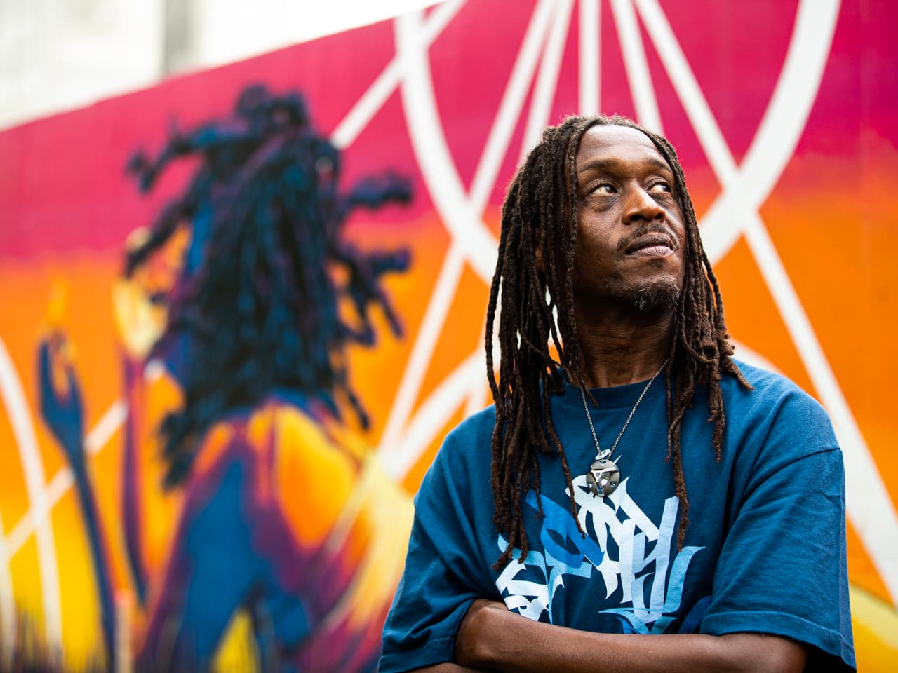 A man stands in front of a colorful mural he painted.