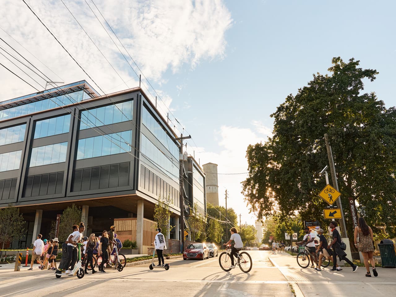 People cross a crosswalk on bikes, scooters, and on foot.