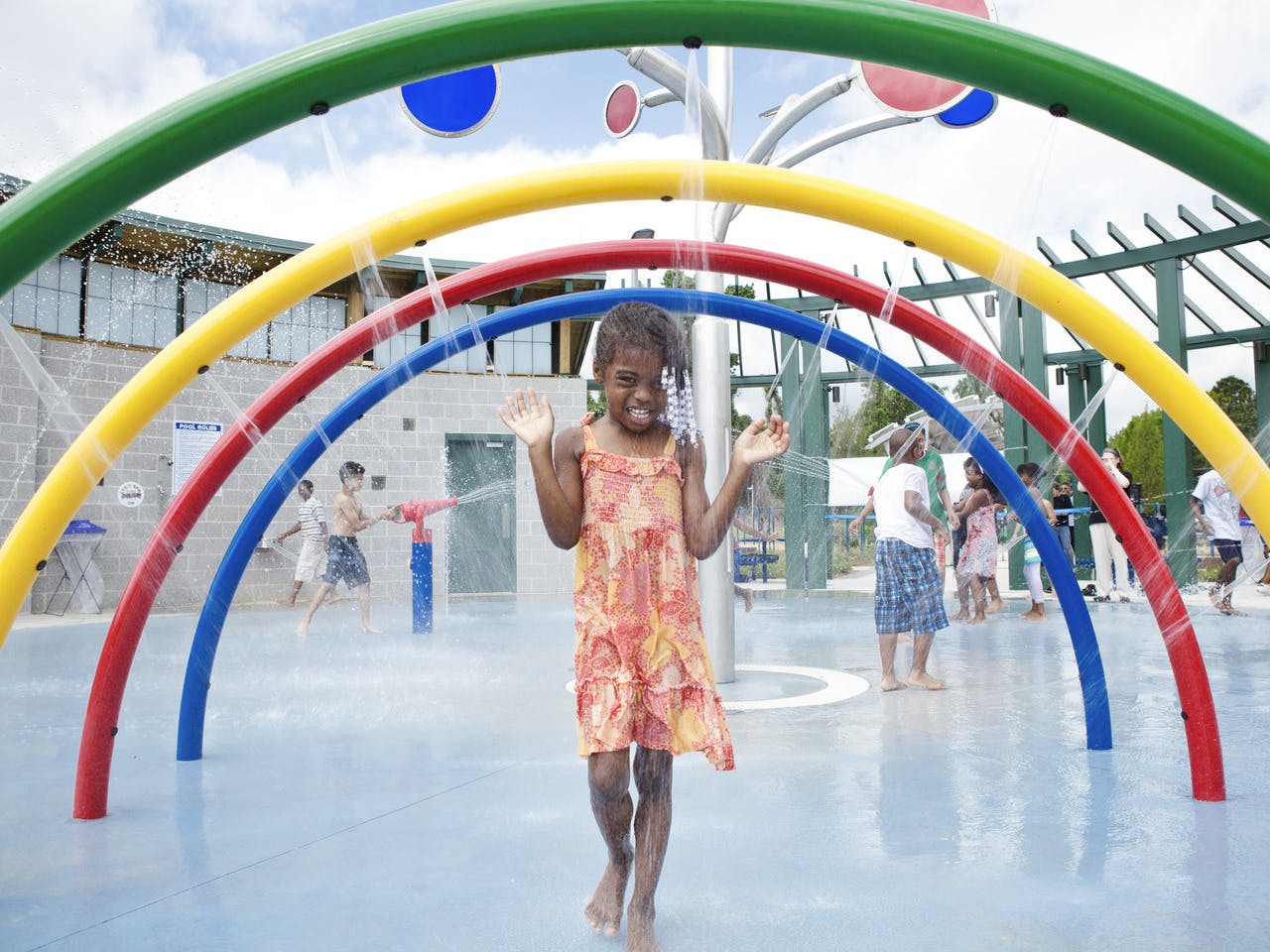 A girl laughs while being sprayed by water on a splash pad.