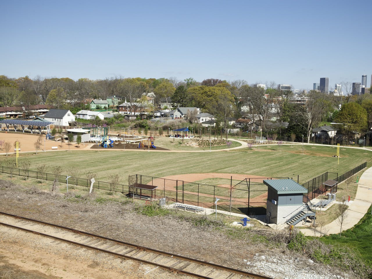 A baseball field sits in front of a playground. The Atlanta skyline is in the back.