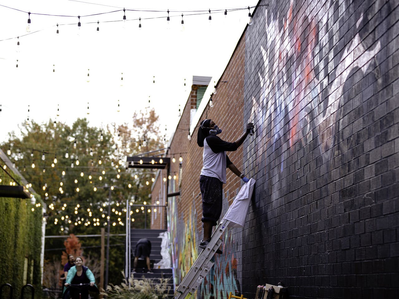 A man paints a brick wall using spray paint.