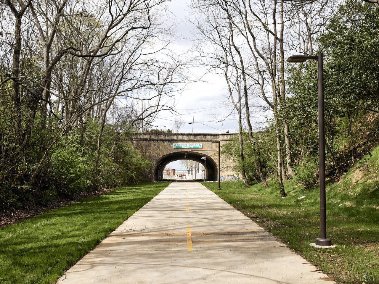 A paved pathway leads under a bridge with grass on both sides.