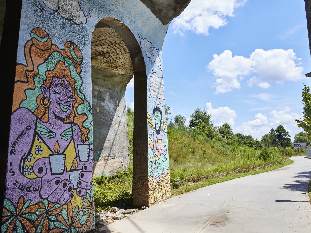 A colorful mural adorns the underside of a bride along a paved path.
