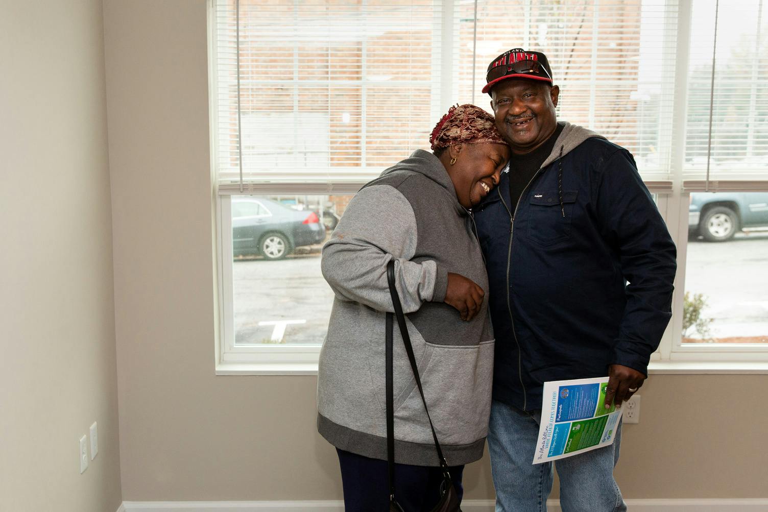 A happy older couple stands in an empty apartment smiling and hugging.