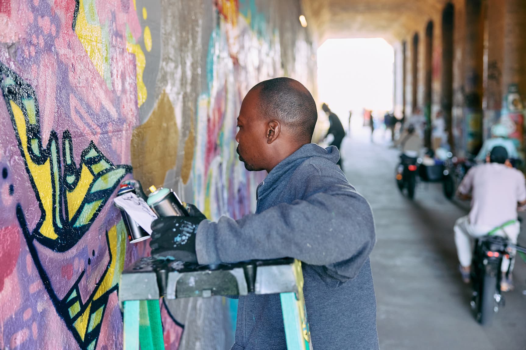 A man stands with a can of spray paint in front of a painted wall he's working on.