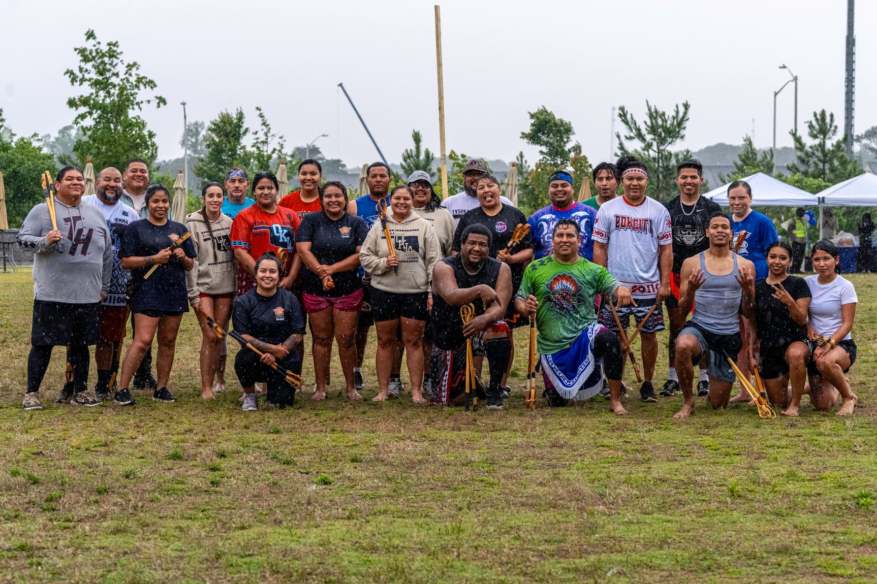A photo of a group of people posing together, holding Toli sticks, and smiling in the rain.