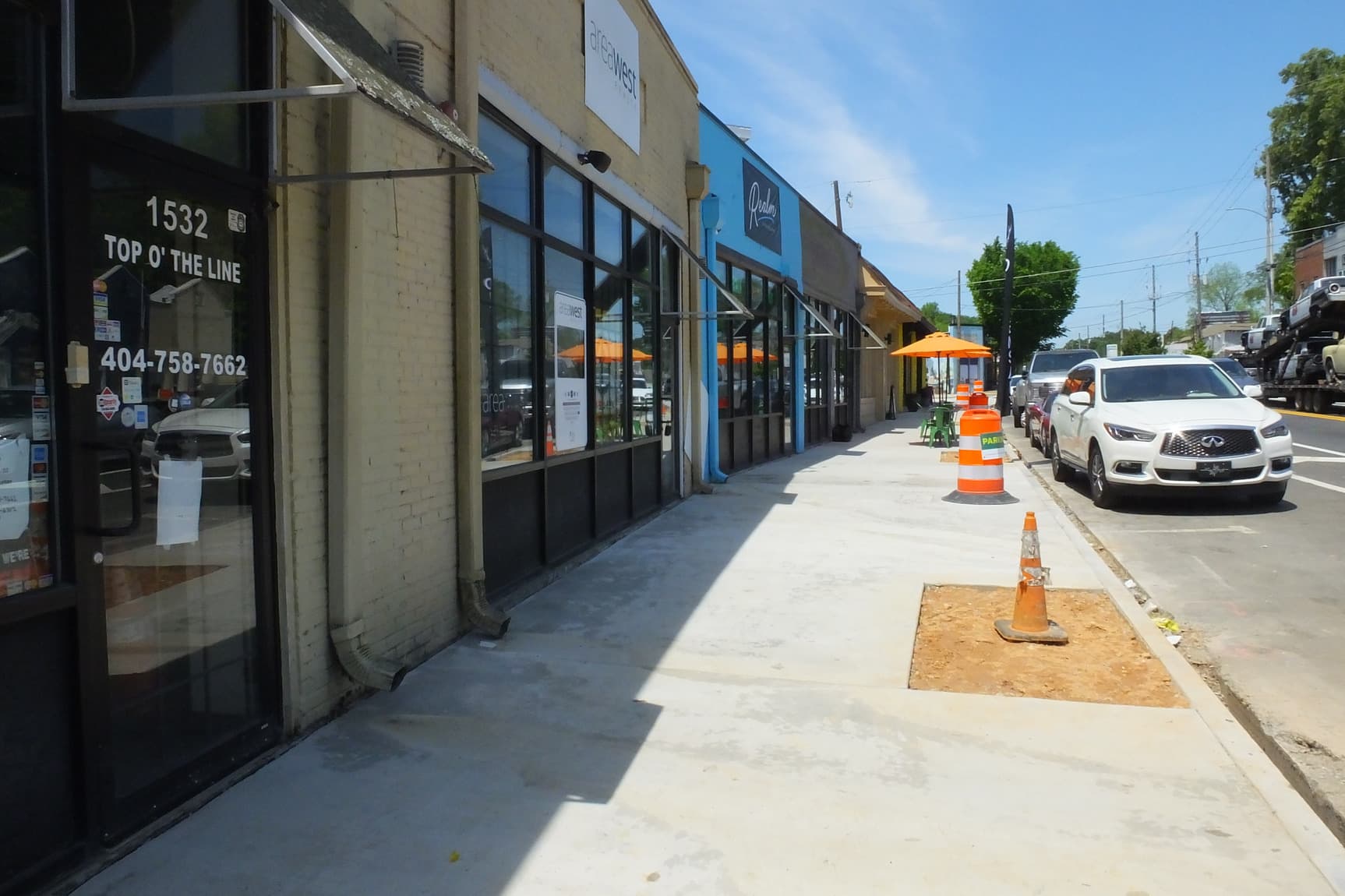 A newly built sidewalk sits between a busy road and a row of small businesses.