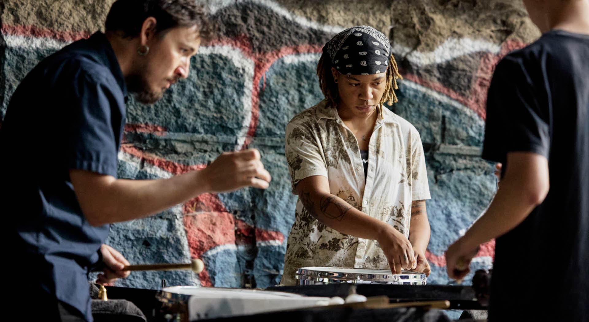 Musical artists perform on drums with the backdrop of a stone tunnel. (Photo Credit: Erin Sintos)