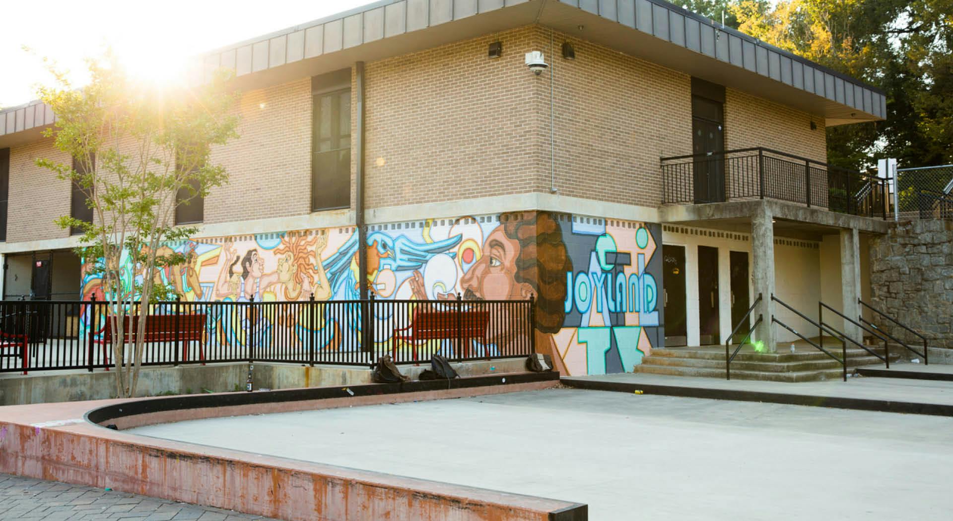 A skate park in front of a building that features a colorful mural honoring the Joyland neighborhood.