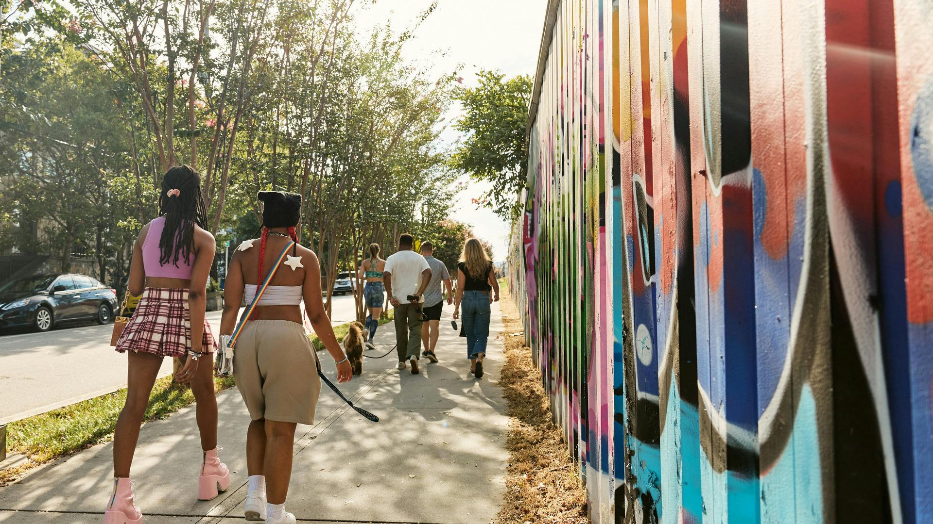Several people walk alongside a mural-filled walls.