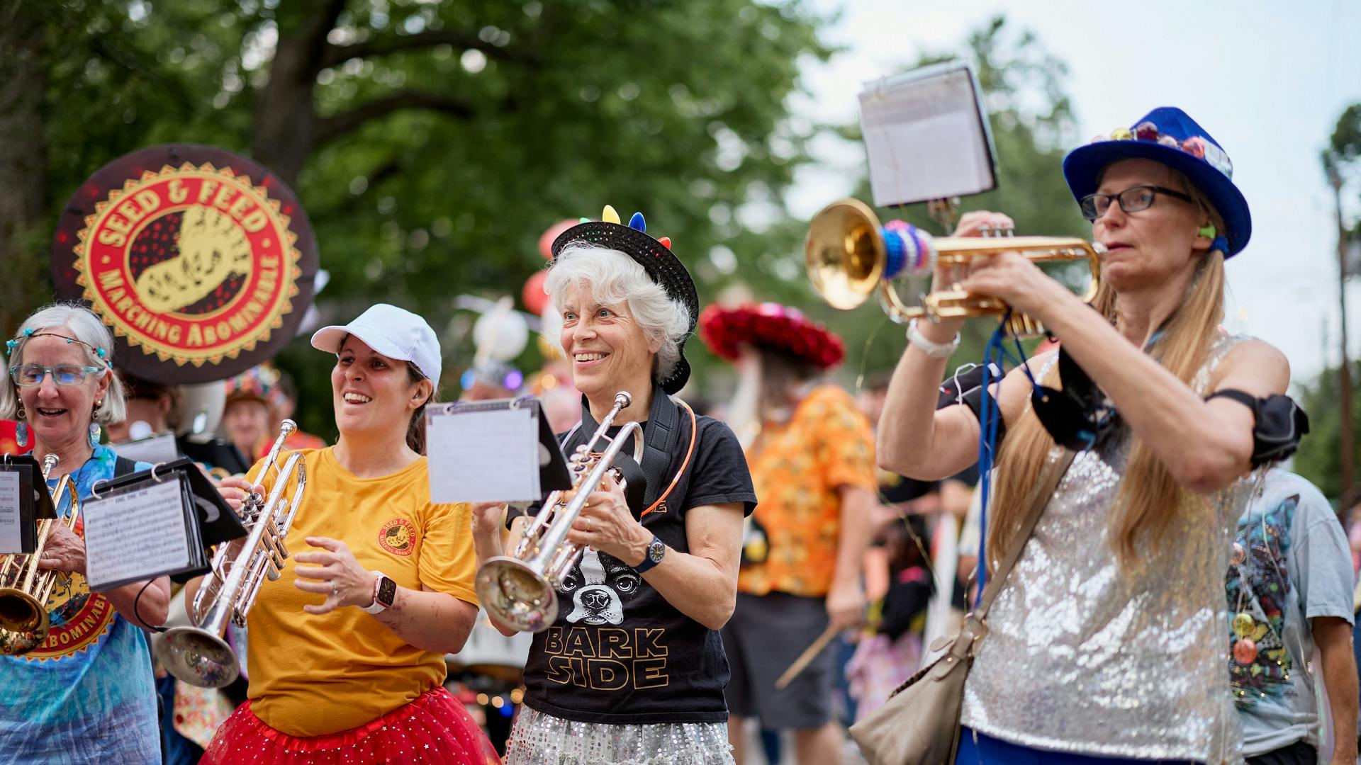 Women with trumpets laugh and play for a crowd.