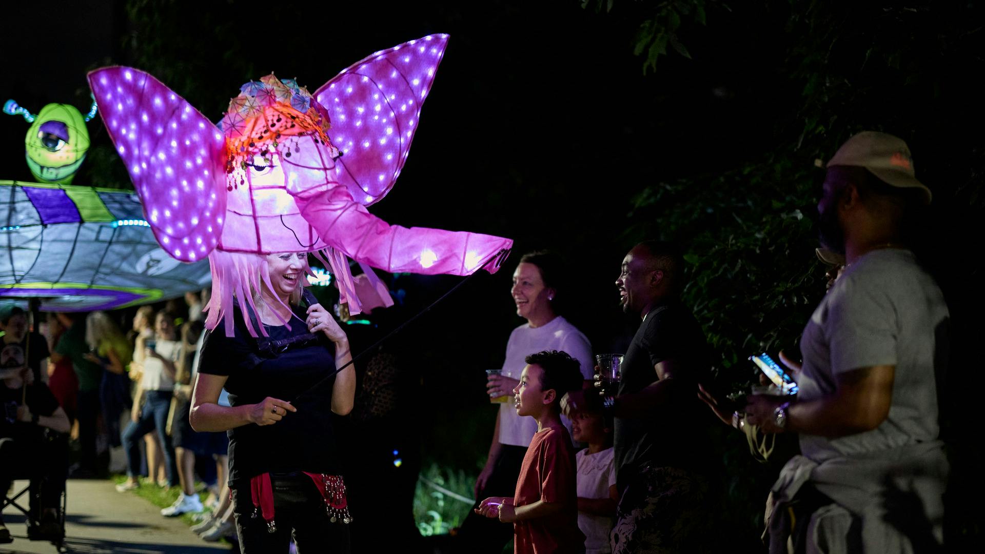 A woman stands in front of a smiling child with a large, illuminated elephant lantern.