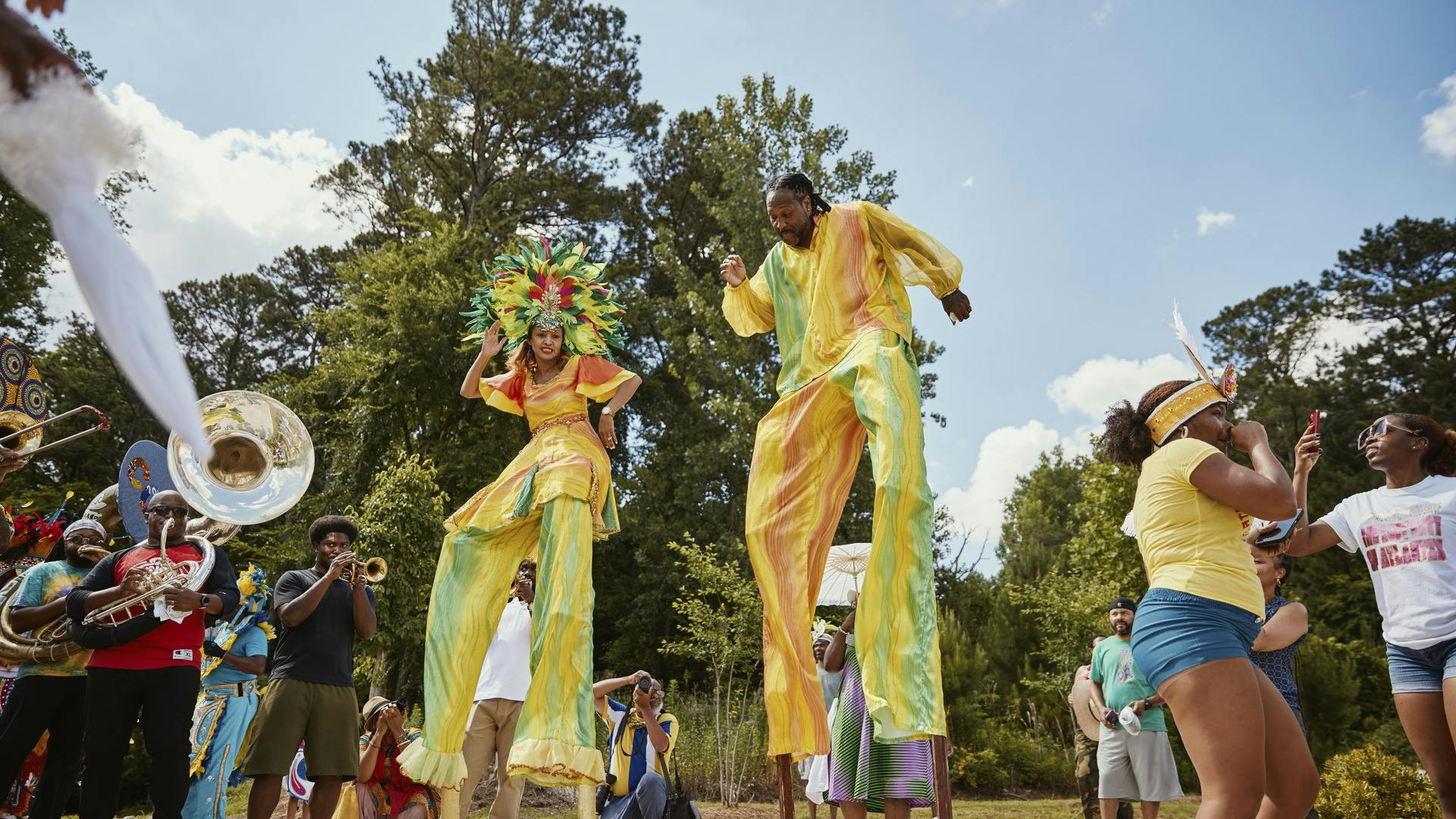 People on stilts in bright outfits perform to music.