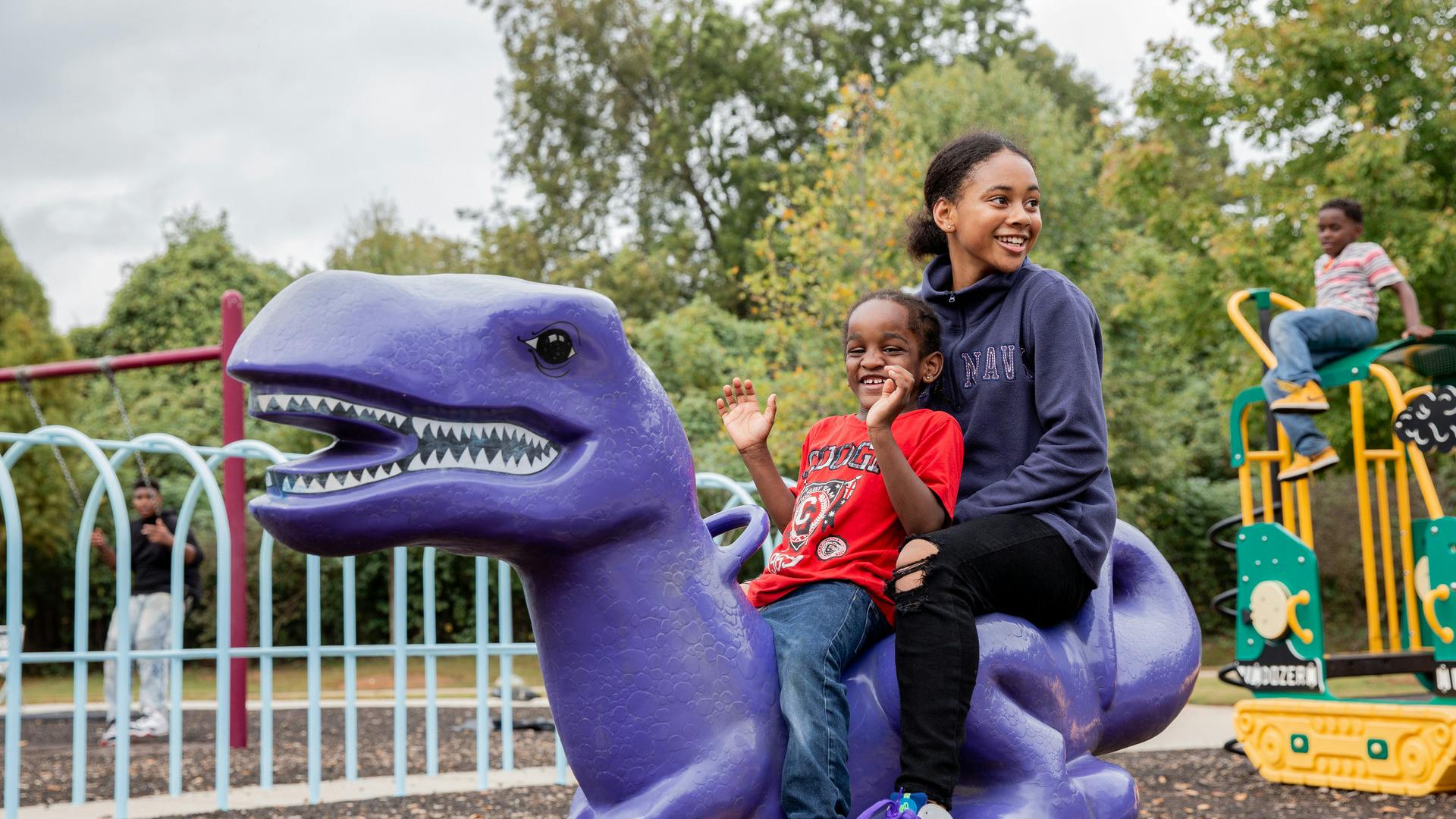Two happy kids sit on the back of a purple plastic dinosaur.