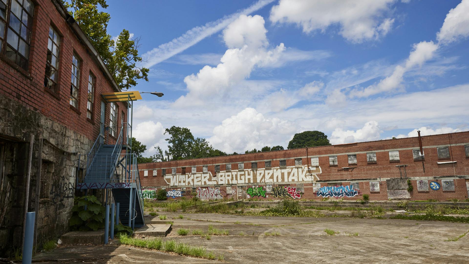 Two abandoned warehouse buildings are shown covered in colorful graffiti.
