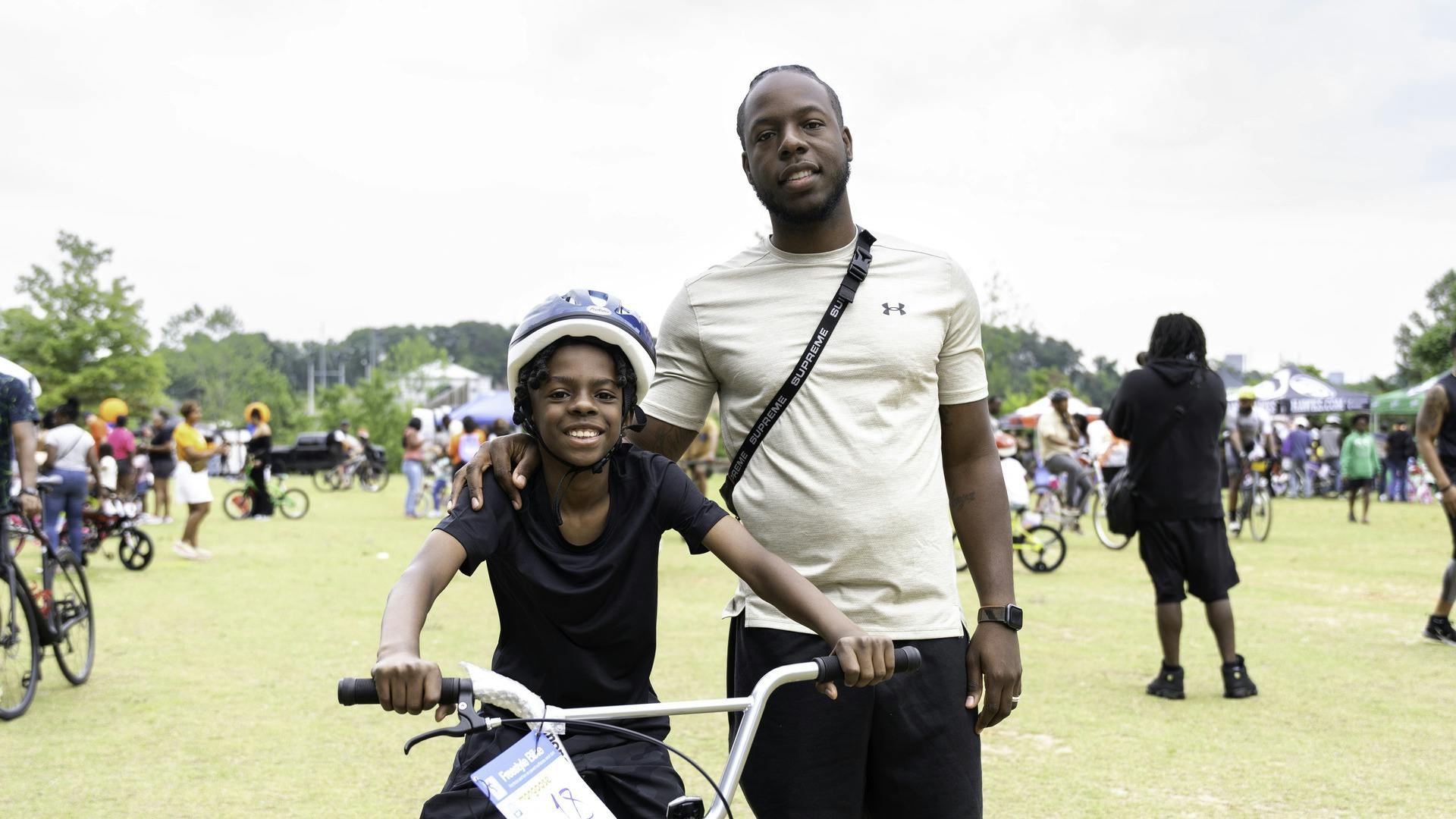 A kid sits on his bike, smiling, with a man smiling next to him.