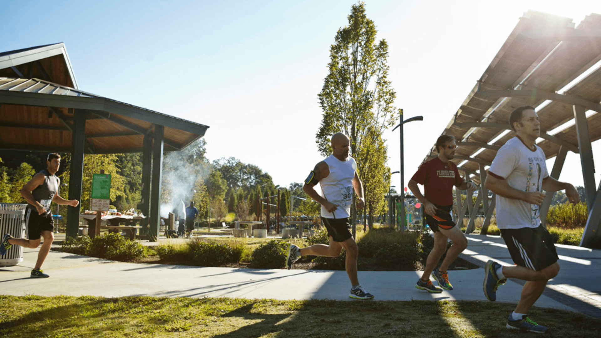 A group of men run along a sidewalk in the sun.