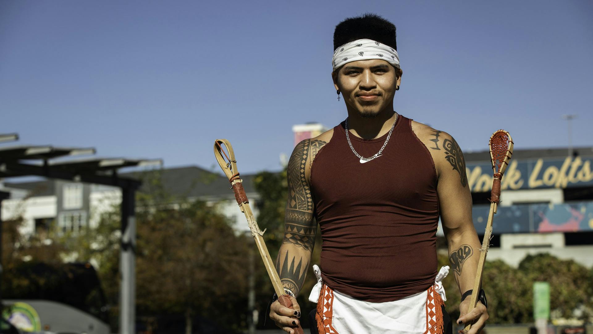 A person stands, holding a Stickball stick in each hand, looking at the camera.