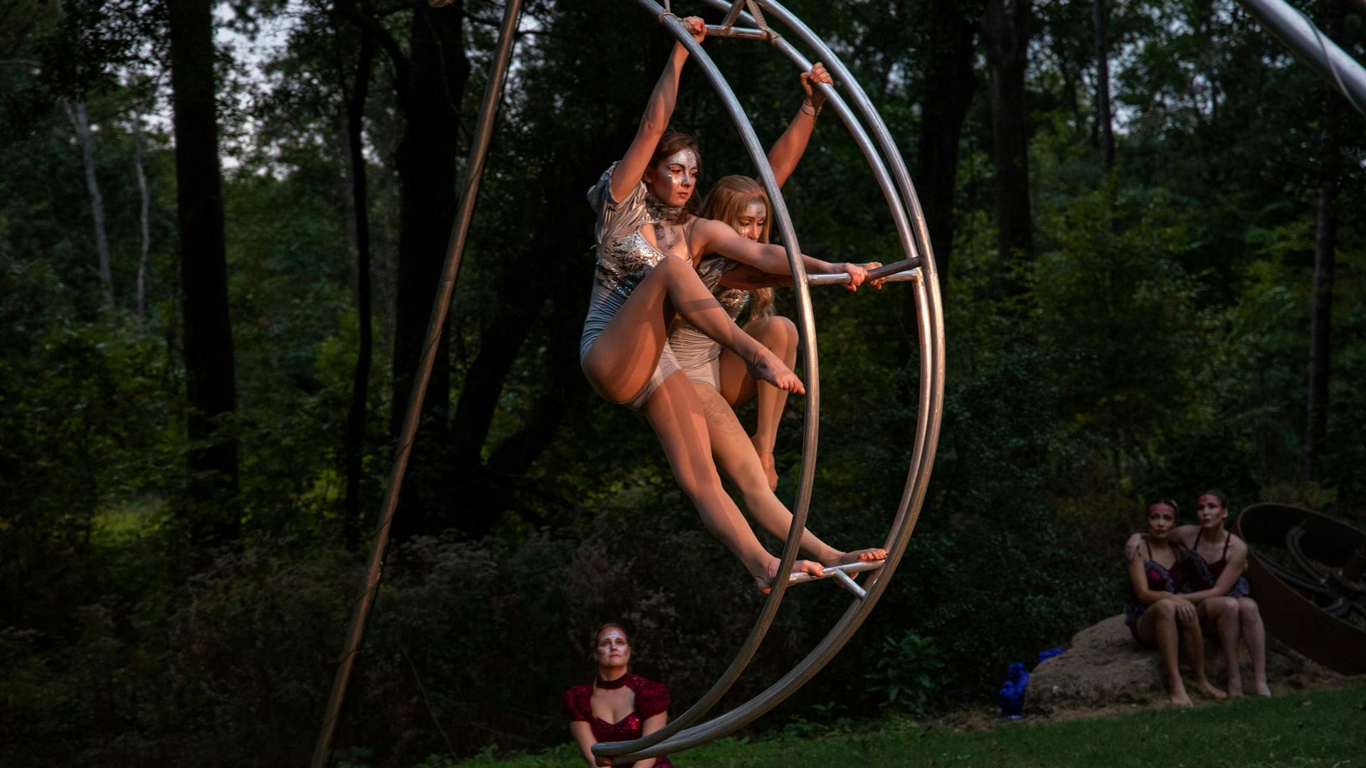 Dancers stand on a rounded metal pole during a performance.
