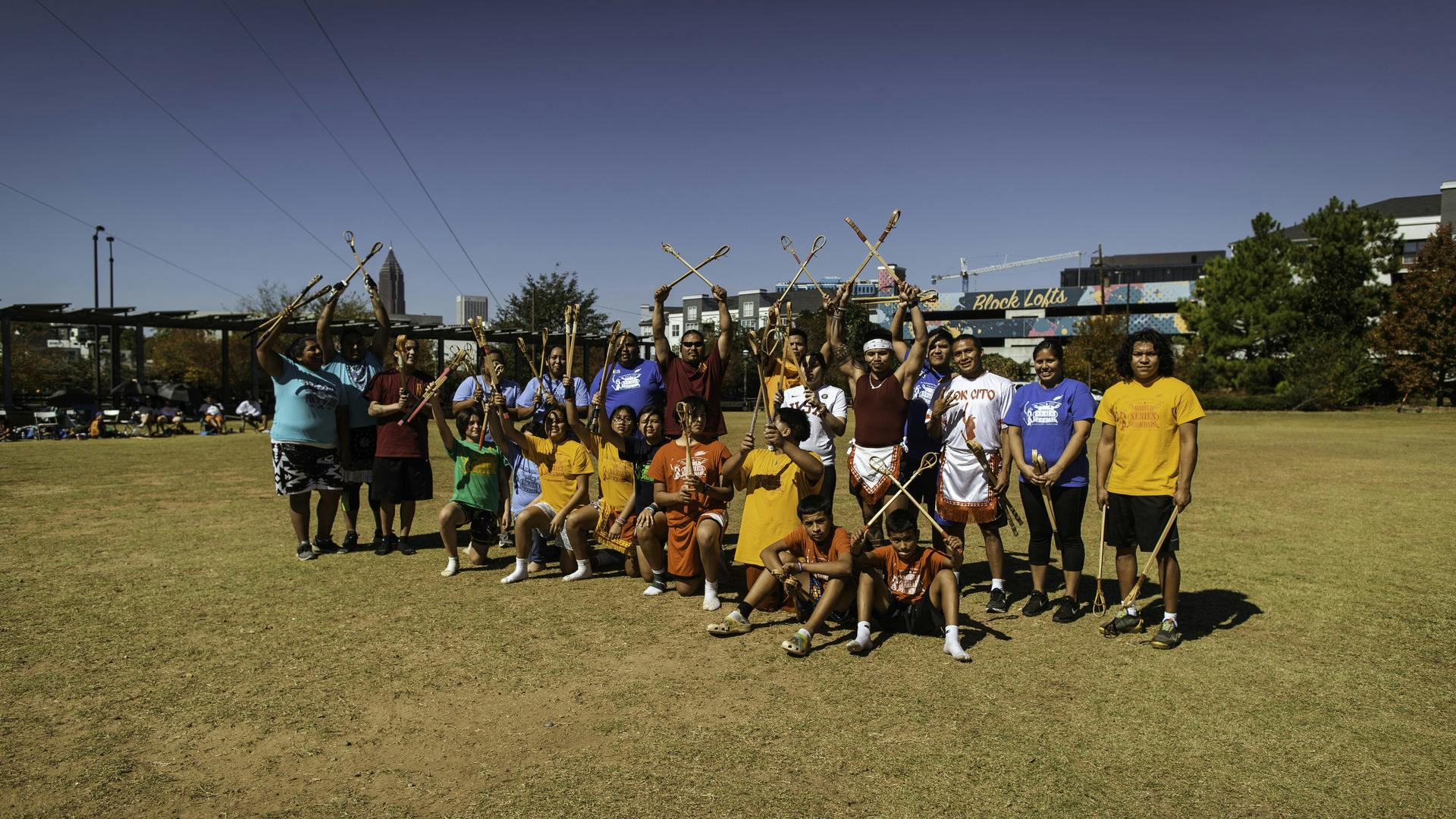 Members of Indigenous Nations pose together for a photo with their Stickball sticks on the activity field at the Historic Fourth Ward Skatepark.