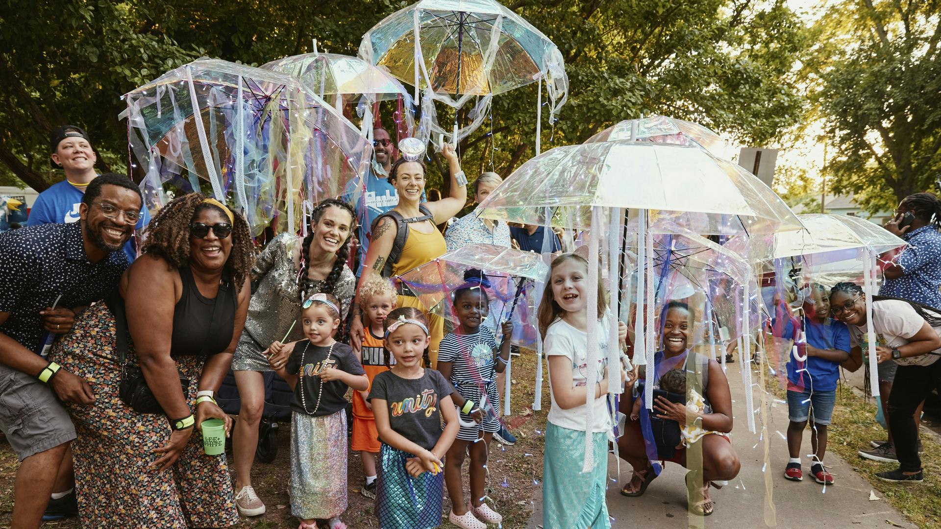 Children and their parents pose, smiling, laughing, and holding colorful parasols.