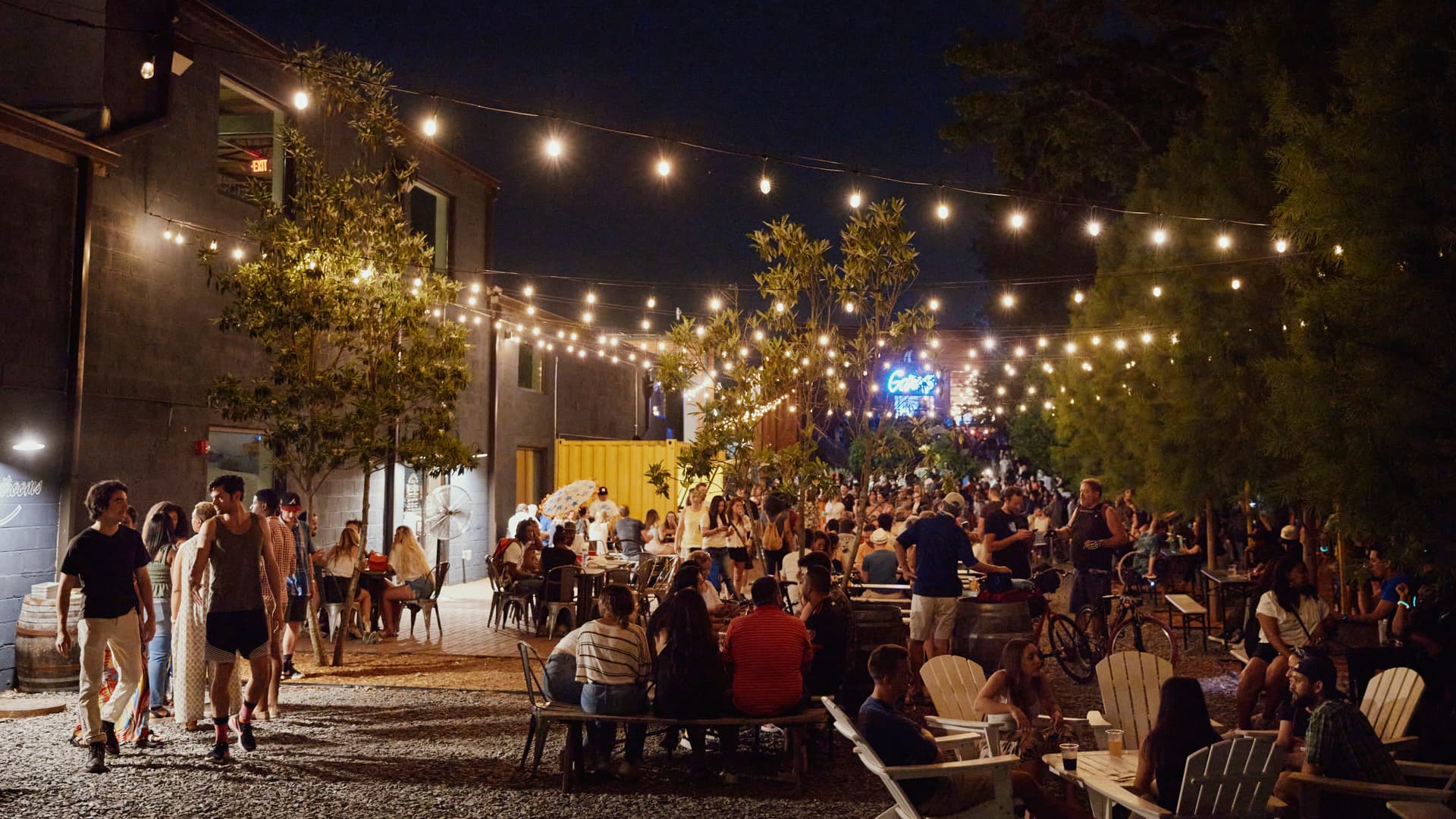 Crowds of people sit in chairs outside of an establishment at night.