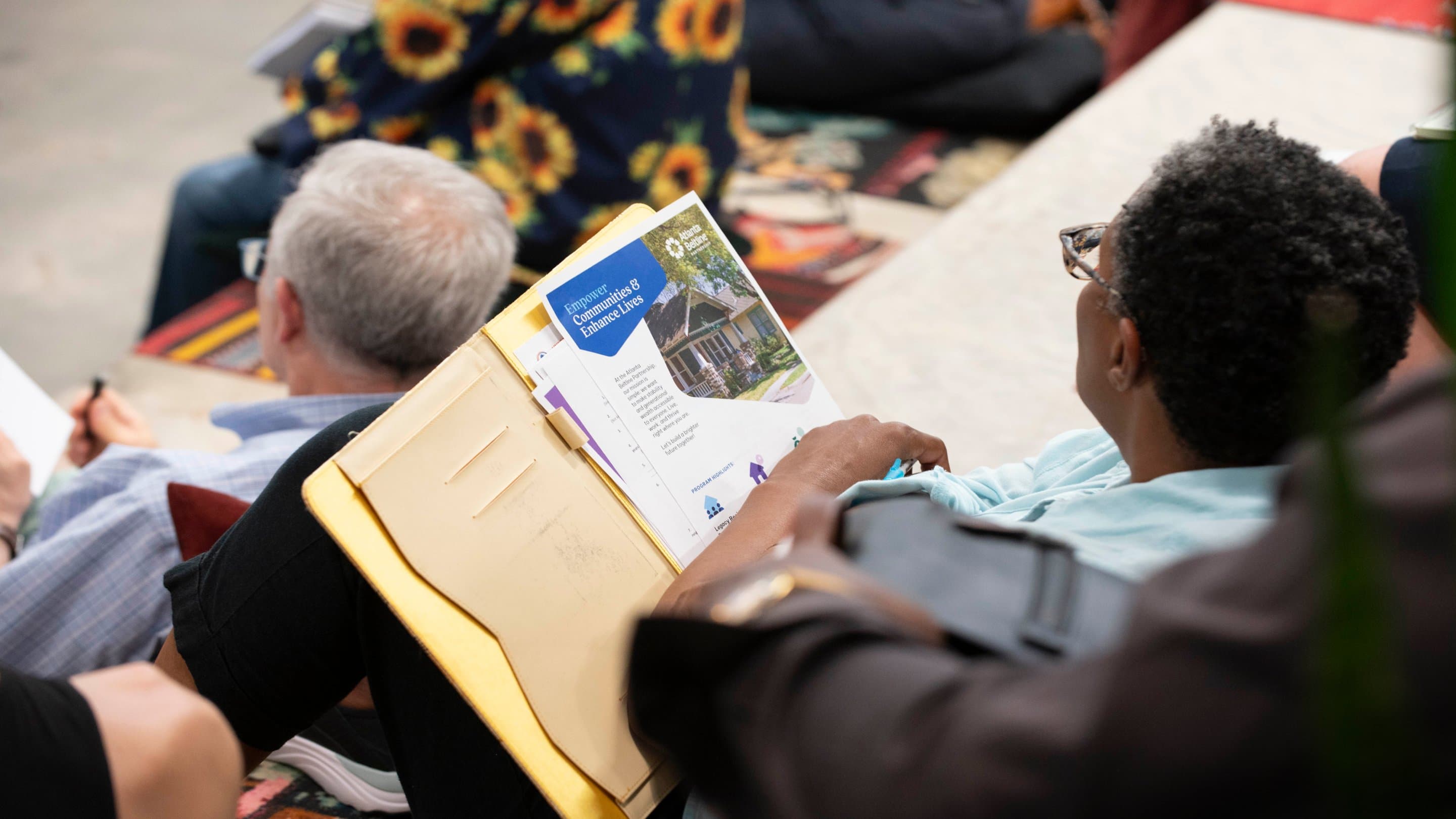 Person reading a pamphlet in a seated crowd.