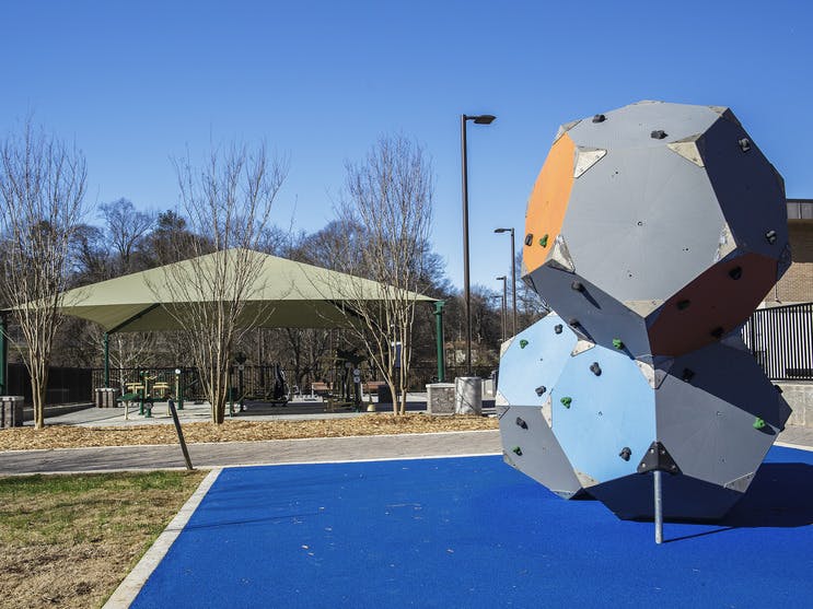 A climbing structure with bright colors stands in the foreground, while outdoor exercise equipment is visible beyond it.