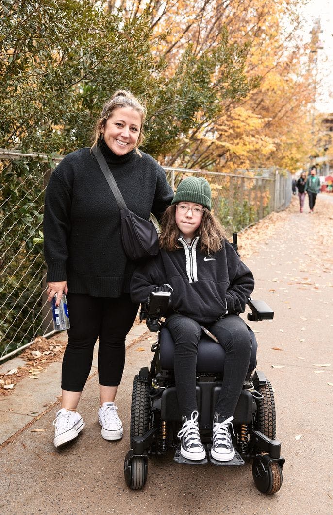 A happy person stands next to someone smiling in a wheel chair.