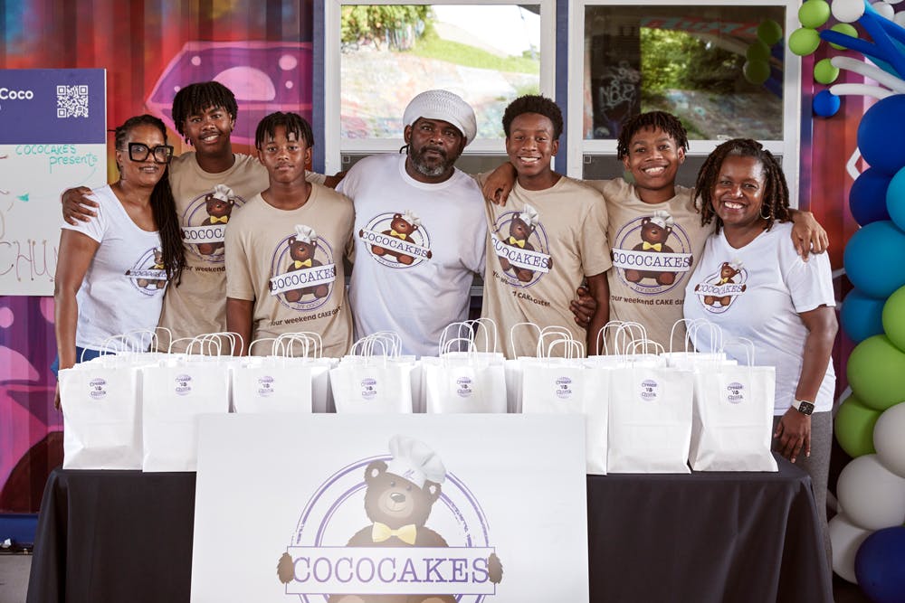 The family and business partners behind CocoCakes by Coco stand behind a table with their baked goods.