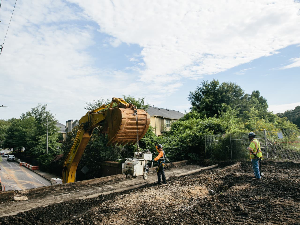 Two people in construction attire guide a piece of machinery at a job site.