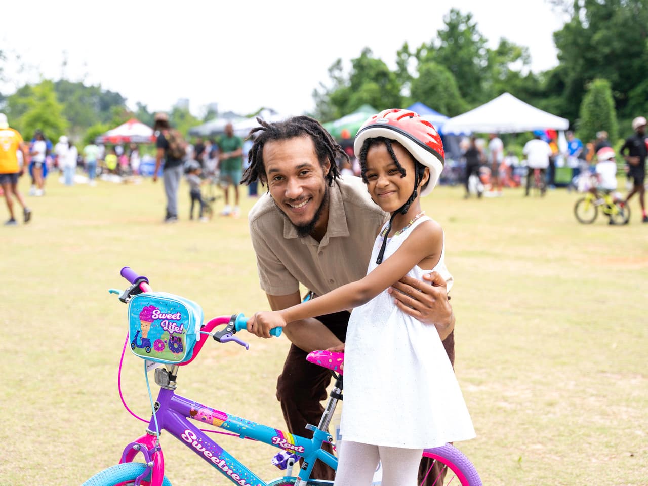 A man and a young girl stand smiling next to a bike.
