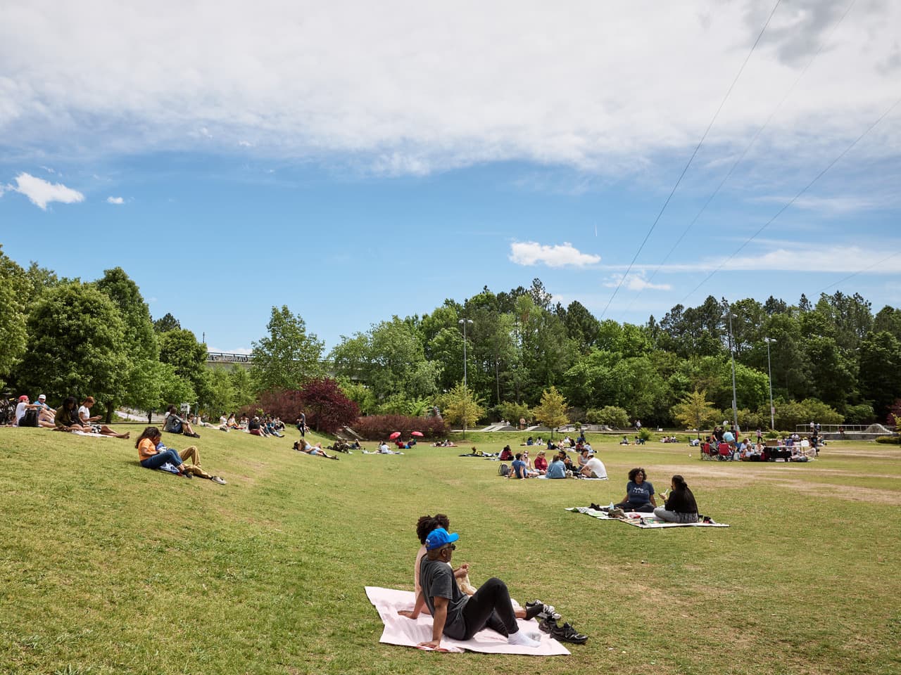 People sit on blankets in groups across a grass activity field on a sunny day.