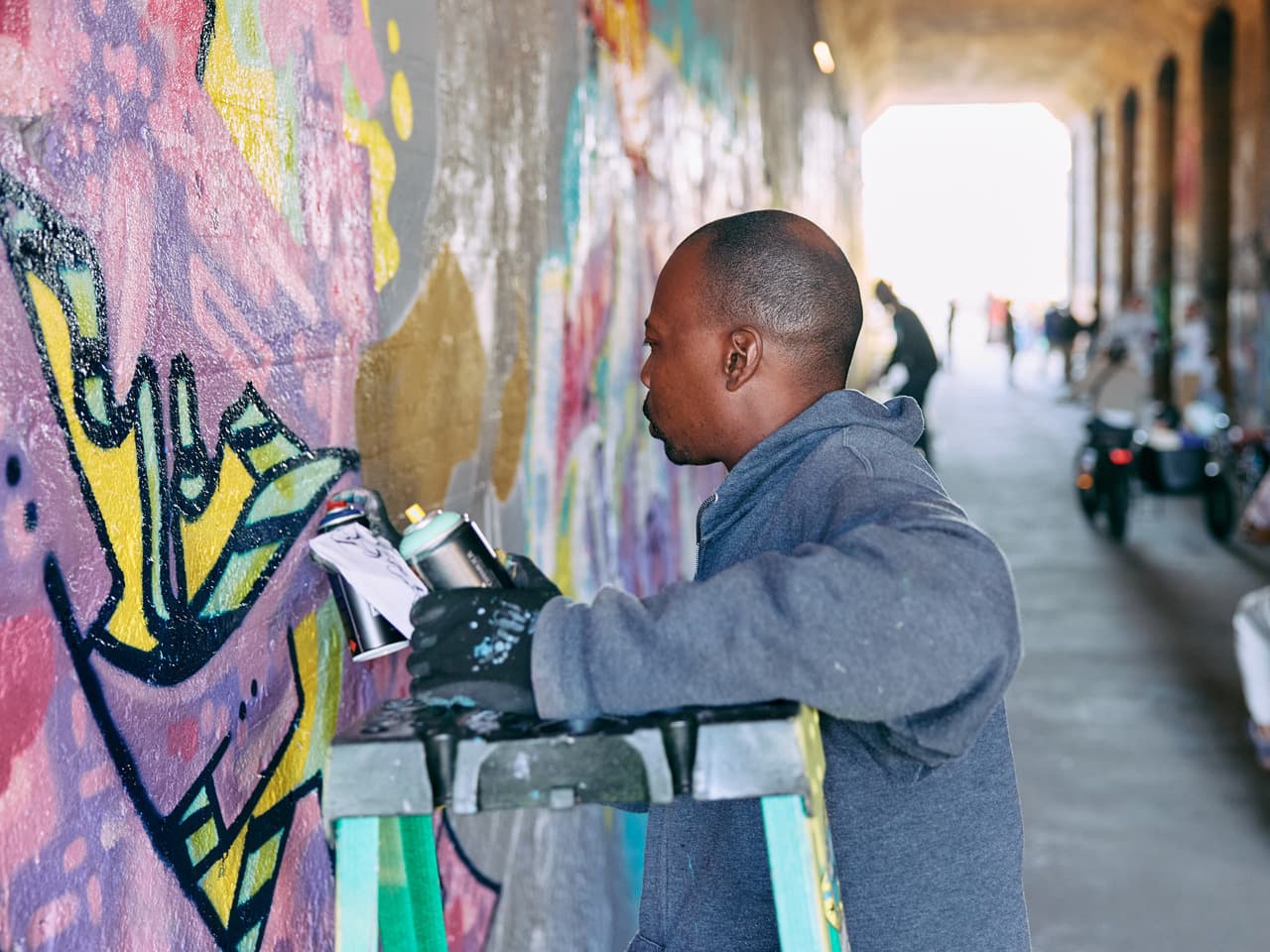 A man stands with a can of spray paint in front of a painted wall he's working on.