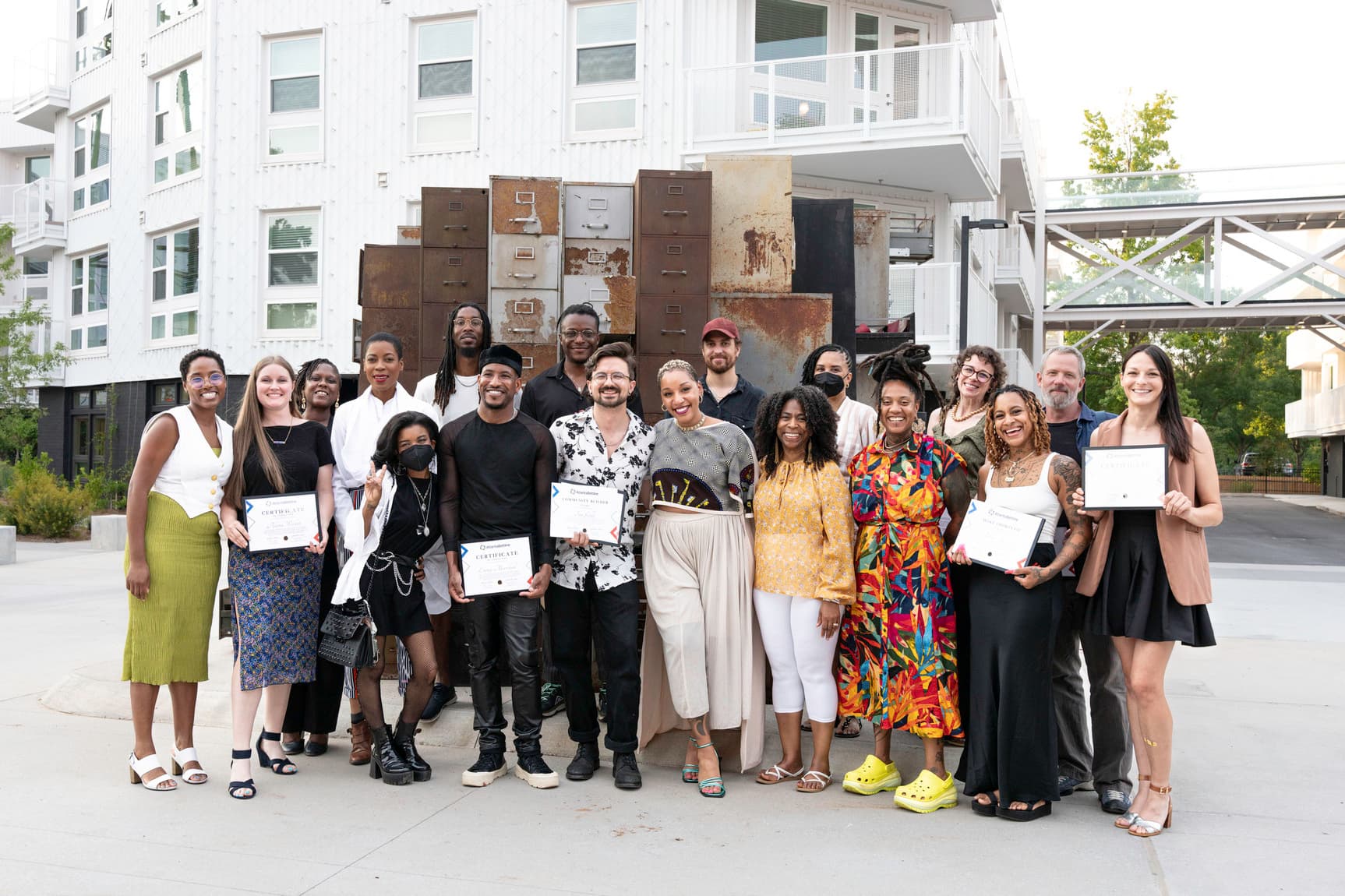 A group of artists pose together outside, smiling and holding graduation certificates.