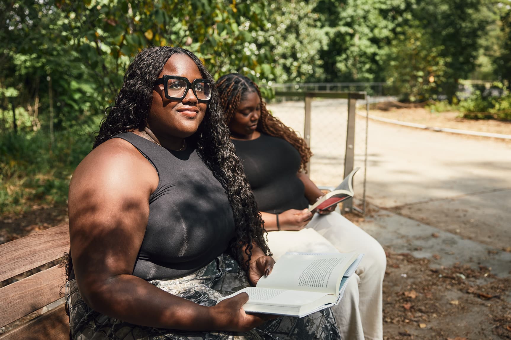 Two people sitting on a bench along the Beltline, reading books. One wears glasses and looks ahead, while the other focuses on the book.