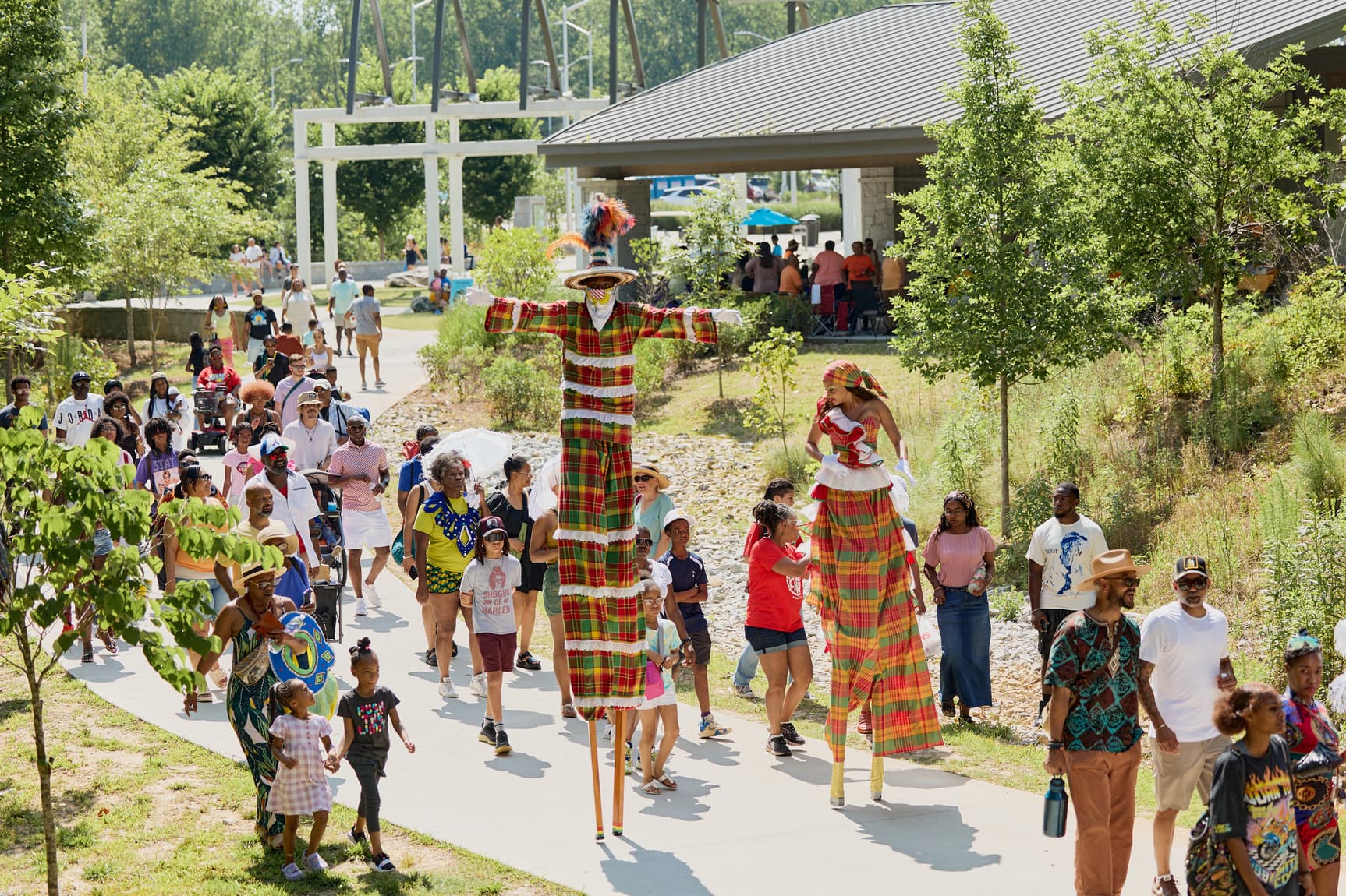 People dressed in costumes walk on stilts among a large crowd of people during a parade through Westside Park.