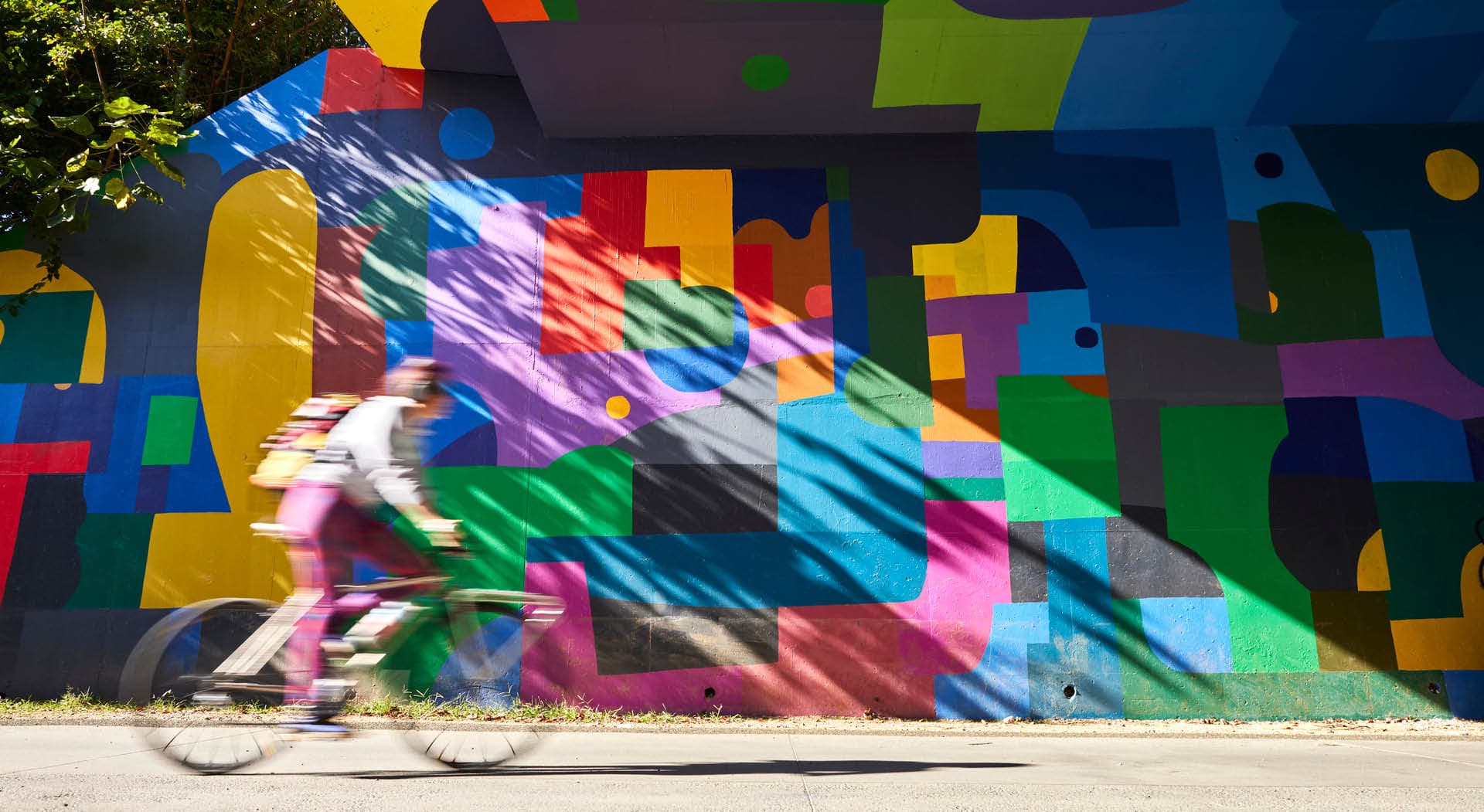 A woman rides her bike in front of a colorful mural by HENSE. (Photo Credit: Erin Sintos)