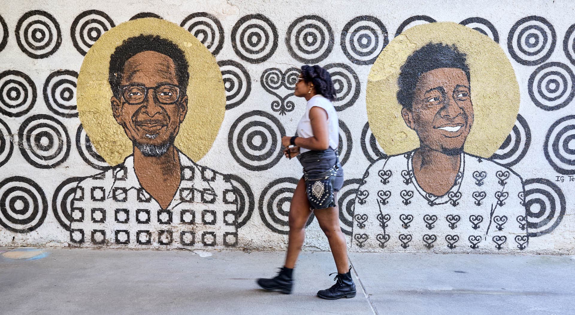 A woman walks in front of a mural titled Storybox painted on the walls of a tunnel and depicting Black figures of Atlanta's Westside communities. (Photo Credit: Erin Sintos)
