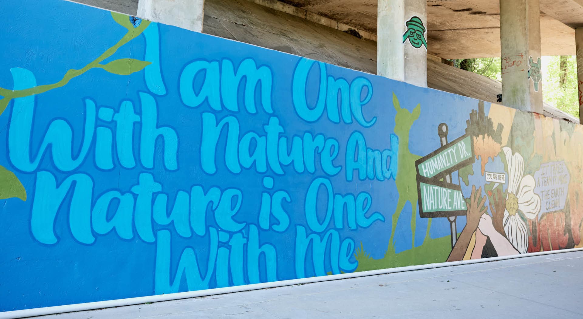 A mural under a bridge with the painted text "I am one with nature and nature is one with me." (Photo Credit: Erin Sintos)