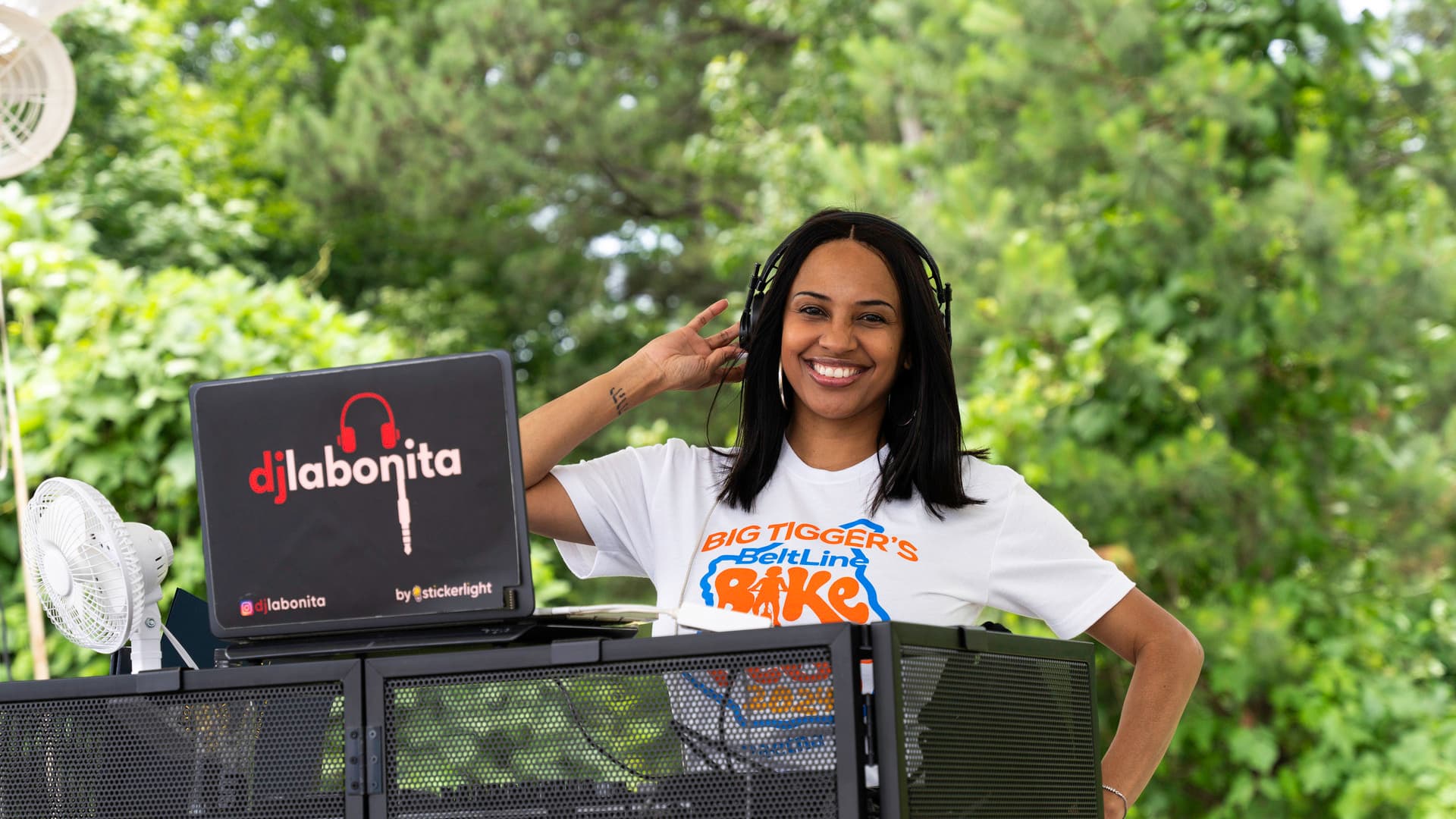 A woman stands at a DJ booth outside.