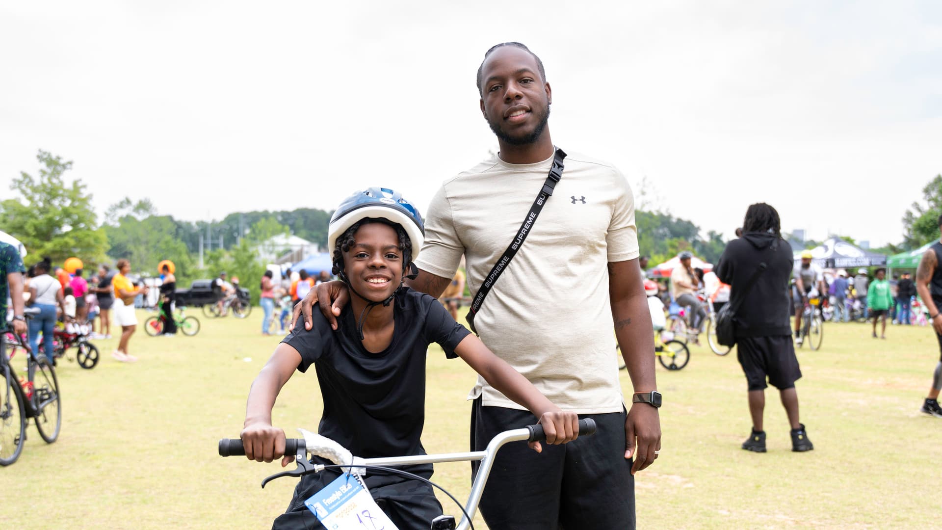 A kid sits on his bike, smiling, with a man smiling next to him.